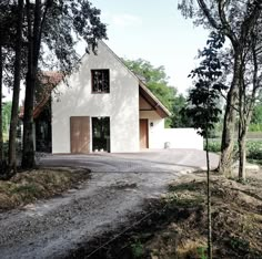 a white house sitting in the middle of a forest next to a dirt road and trees