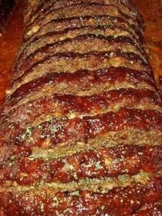 sliced meatloaf sitting on top of a wooden cutting board with sauce and seasoning