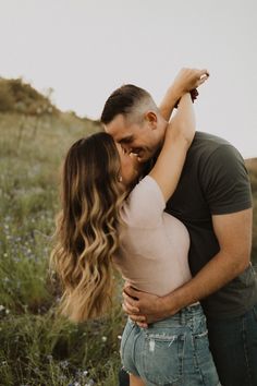 a man and woman embracing each other in the middle of a field with wildflowers