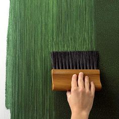 a person is painting the wall with green paint on it and brush being held up by someone's hand