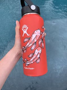 a hand holding a red water bottle with two fish on it and the words hydro flask