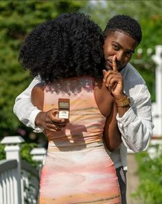 a man and woman standing next to each other looking at something on their cell phone