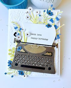 a birthday card with an old fashioned typewriter and blue flowers on the bottom, next to a bottle of wine