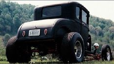 an old black truck parked on top of a lush green field next to a forest