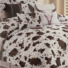 a bed covered in brown and white cow print sheets with pillows on top of it