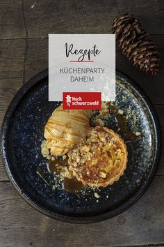 a black plate topped with pancakes covered in toppings next to a pine cone on top of a wooden table