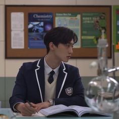 a young man sitting at a table with an open book in front of him and looking to the side