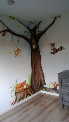 a room with a tree painted on the wall and animals hanging from it's branches