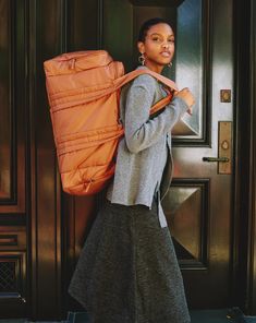 a woman carrying a large orange bag in front of a door