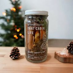 a glass jar filled with food next to a pine cone and christmas tree in the background