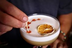 a person is holding a drink with an orange garnish on the rim and a toothpick sticking out of it