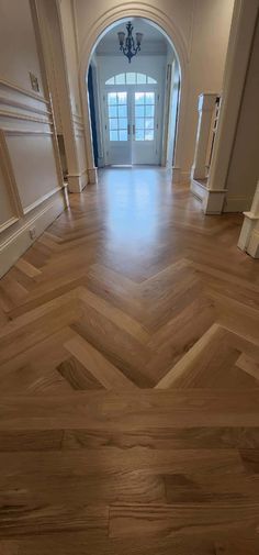 an empty hallway with wooden floors and white trim on the walls, leading to a double doored entryway