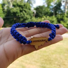 a hand holding a blue bracelet with the word hondura on it and a wooden state map