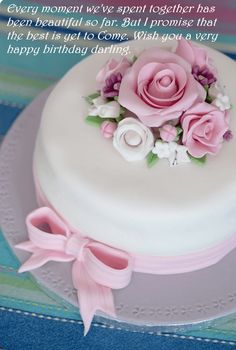 there is a white cake with pink flowers on top and ribbon around the edges,