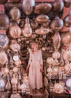 a woman standing in front of a large amount of silverware hanging from the ceiling