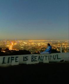 a person sitting on top of a hill with the city lights in the back ground