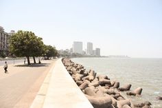 a person walking along the edge of a large body of water with buildings in the background