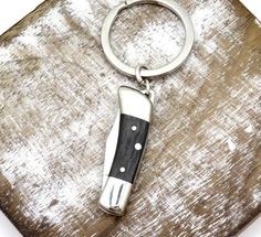 a knife shaped keychain sitting on top of a piece of wood with a metal ring