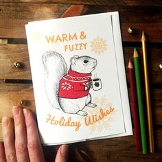 a hand holding a card with an image of a squirrel wearing a sweater and holding a coffee cup