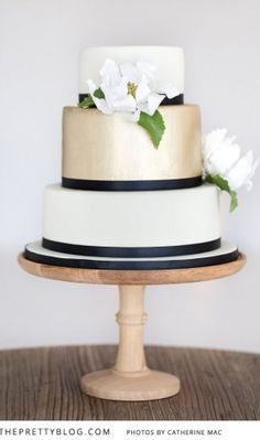 a three tiered cake with white flowers on the top and black trimmings