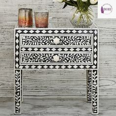 an ornate black and white chest of drawers next to a vase with flowers on it