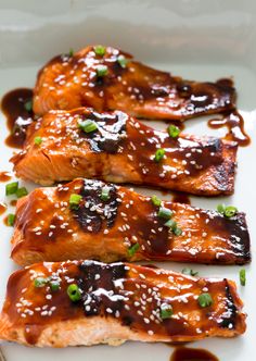 three pieces of salmon covered in sauce and green onions