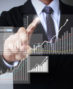 a man in a suit and tie is pointing to an upward graph on the screen