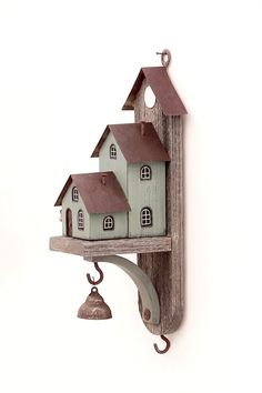 a bird house hanging on the side of a wall with a bell attached to it