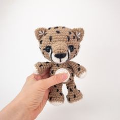 a hand holding a small crocheted teddy bear in front of a white background