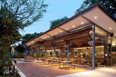 an outdoor dining area with tables and chairs under a canopy at night, surrounded by greenery