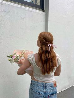 a woman with red hair is holding flowers and looking out the window at something outside