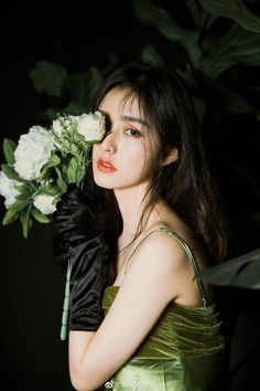 a woman in a green dress holding flowers and wearing black gloves with her hand on her face