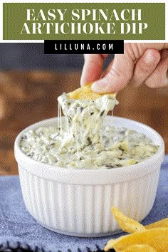 a hand dipping a chip into a bowl of artichoke dip