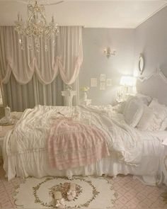 a white bed sitting under a chandelier in a bedroom next to a window