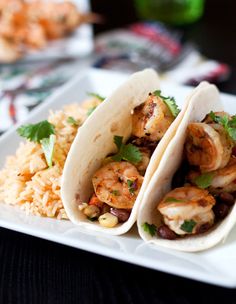 two shrimp tacos on a plate with rice and cilantro