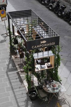 an outdoor cafe with plants growing out of it's roof and on the sidewalk