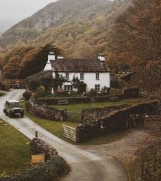 a car driving down a country road next to a white house with mountains in the background