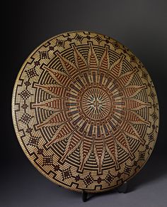 a brown and black plate with designs on the inside, sitting on a stand in front of a dark background