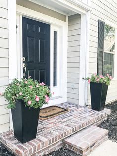 two black planters with pink flowers are on the front step of a house,