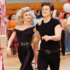 a man and woman dressed in black are dancing on the dance floor with balloons behind them