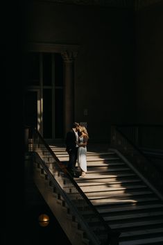 a man and woman standing on top of a stair case next to each other in the dark