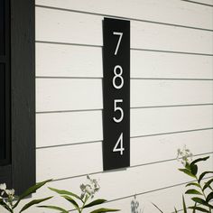 a house number sign mounted to the side of a white building with flowers in front of it