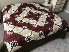 a bed with a red and white quilt on it's cover next to a night stand