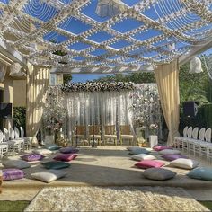 an outdoor wedding venue with white chairs and lots of pillows on the floor, covered in curtains