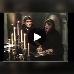 two men standing next to each other with candles in front of them and one man holding a book