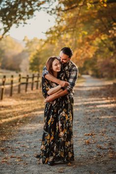 a man and woman hugging each other in the middle of a dirt road surrounded by trees