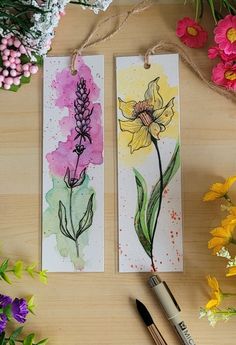 two tags with watercolor flowers on them next to some paintbrushes and markers