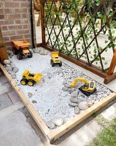 toy construction vehicles are set up in a graveled area near a brick wall and trellis