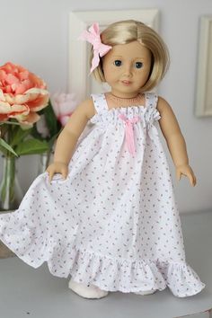 a doll with blonde hair wearing a white dress and pink bow in front of flowers