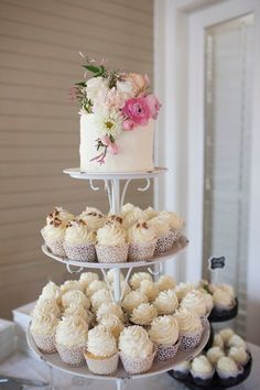 a three tiered cake and cupcakes on a table